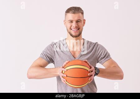 Porträt eines fröhlichen Basketballspielers, der Ball in den Händen trägt und lächelt, während er auf weißem Hintergrund isoliert ist. Fröhlicher bärtiger Flusspferd, der mit BA trainiert Stockfoto