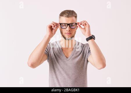 Vorderansicht des jungen Business-Experten, der Brille trägt und nach einer Kamera sucht, während er auf weißem Hintergrund isoliert ist. Attraktiver und charmanter Flusspferde c Stockfoto