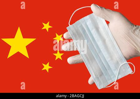 Doktor hält die medizinische Gesichtsmaske in weißen Handschuhen auf der chinesischen Flagge mit Hintergrundfarben in der Hand. Konzept Pandemieversicherung Coronavirus, durch die Luft übertragbare Krankheiten Stockfoto