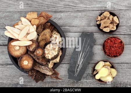 Chinesische Kräuter und Akupunkturnadeln, die in der traditionellen Kräutermedizin auf rustikalem Holzhintergrund verwendet werden. Stockfoto