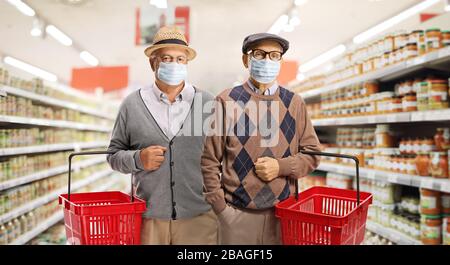 Zwei Seniorinnen tragen medizinische Gesichtsmasken und halten Einkaufskörbe in einem Supermarkt Stockfoto