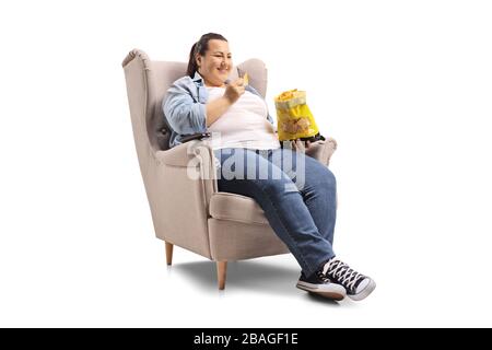 Übergewichtige Frau, die in einem Sessel sitzt und Tortilla-Chips isst, isoliert auf weißem Hintergrund Stockfoto