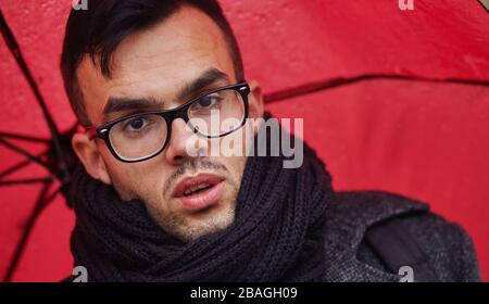 Der Geschäftsmann geht mit rotem Regenschirm in den Regen Stockfoto