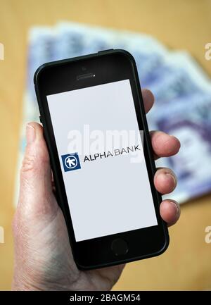 Eine Frau, die das Logo der Alpha Bank auf einem Mobiltelefon betrachtet. (Nur redaktionelle Verwendung) Stockfoto