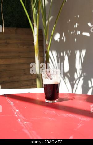 Ein halbes Pint Guinness auf einem Tisch draußen in der Sonne. Stockfoto