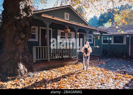 Eine Frau mit Kind steht neben einem Haus auf gelben Blättern Stockfoto