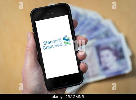 Eine Frau, die das Logo der Standard Chartered Bank auf einem Mobiltelefon betrachtet. (Nur redaktionelle Verwendung) Stockfoto