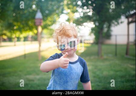 Junge, die einen Daumen nach oben mit Sonnenbrille auf Stehen im Hinterhof Stockfoto