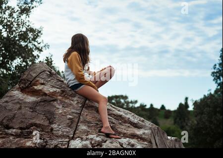 Junges Mädchen 10-12 Jahre alt Blick auf Wolken während auf einem Holzstamm sitzen Stockfoto