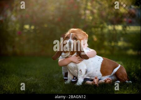 Kleinkind Junge sitzt und umarmt seinen Hund im Hinterhof Gras Stockfoto