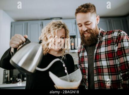 Lächelndes junges Paar macht gießen über Kaffee in ihrer Küche Stockfoto