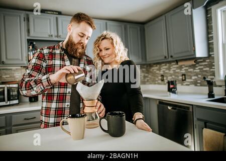 Mann mit Bart und Frau machen über Kaffee zusammen in ihrer Küche Stockfoto