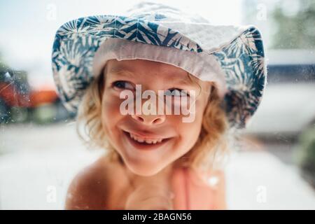 Kleiner Junge mit glattgestameltes Gesicht im Fenster trägt Eimer Hut Stockfoto