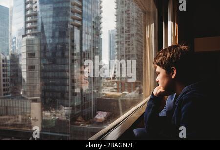 Zwischen Jungen, der aus einem Fenster auf hohe Gebäude der Stadt draußen schaut. Stockfoto