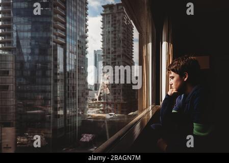 Zwischen Jungen, der aus einem Fenster auf hohe Gebäude der Stadt draußen schaut. Stockfoto