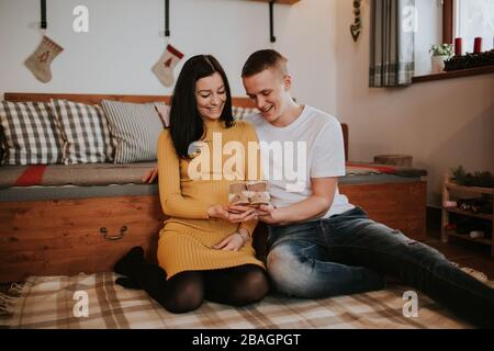Junge schwangere Frau und Mann mit Babystiefeln. Liebevolles junges Paar erwartet ein Baby, das auf dem Boden sitzt und lächelt. Stockfoto