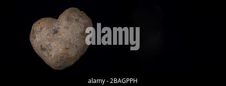 Herzförmige Kartoffel auf schwarzem Grund Stockfoto