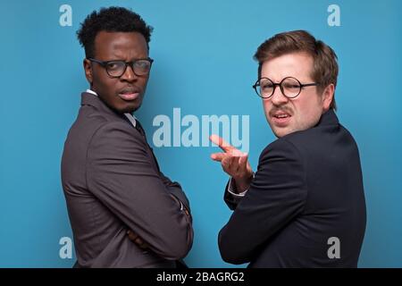 Zwei Männer haben sich beschwert und streiten mit dem Geschäftspartner. Verärgerte und verärgerte Jungs in Anzügen heben eine Hand frustriert und verblüfft, starre verwirrt, ca Stockfoto