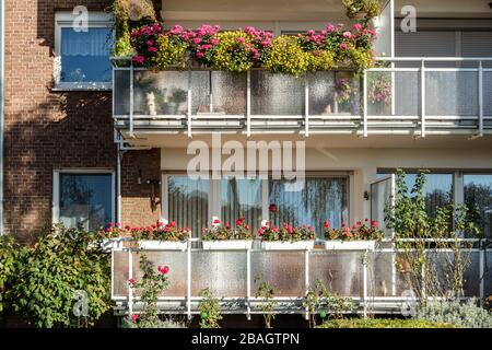 Traditionelles europäisches Wohnhaus mit Balkonen mit bunten Blumen und Blumentöpfen. Fassade eines Wohnhauses mit gepflegten Loggien und Stockfoto