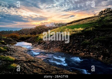 Ruhiger Gebirgsfluss, der unter einem amüsierenden Sonnenuntergang verläuft. Stockfoto