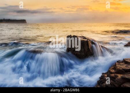 Großer Felsbrocken, der bei Sonnenaufgang an den Nordstränden von Sydney von großer Meereswelle überrollt wurde. Stockfoto