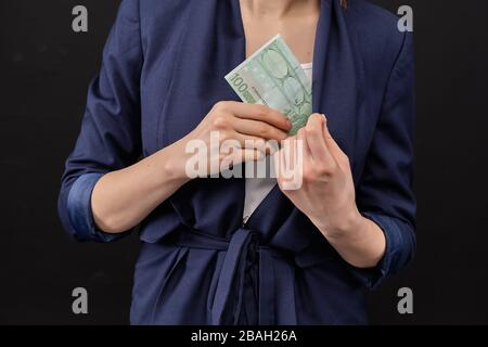 Mädchen in einer Jacke entfernt Euro-Scheine in seiner Tasche auf schwarzem Hintergrund. Nahaufnahme. Stockfoto