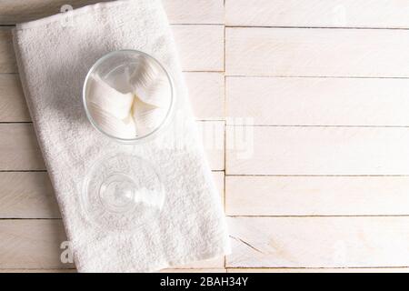 Dekorativer Glasbecher mit Baumwollpolstern und Handtuch auf dem Tisch vor Holzhintergrund. Leerzeichen für Text Stockfoto