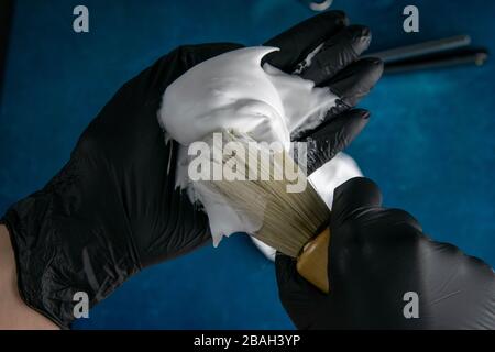 Die Hand hält die Bürste für das Auftragen von Schaum auf Bart, Schaum und gefährlichem Rasiermesser auf blauem Hintergrund. Friseurkonzept Stockfoto