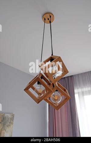 Ursprünglicher Deckenleuchter, Holzwürfel und Lampen im Inneren. Quadratischer Kronleuchter an der Decke im Raum. Stockfoto