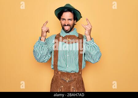 Junger gutaussehender Mann, der tratidionale deutsche oktoberfest-hüter für das Deutschlandfestival trägt, schreit mit verrücktem Ausdruck Rock-Symbol mit Händen nach oben. Stockfoto