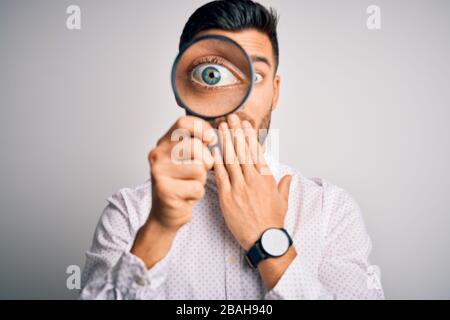 Junger Detektivmann, der mit der Hand schockiert aus versehen, Ausdruck der Angst, durch Lupe über den isolierten Hintergrundeöffnung blickt Stockfoto