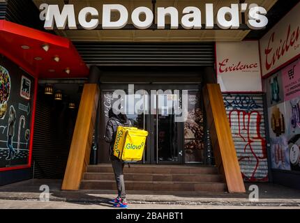 Bukarest, Rumänien - 25. März 2020: Ein Glovo-Kurier für die Lebensmittelzustellung steht vor dem ältesten McDonald's-Restaurant in Rumänien, das vorübergehend geschlossen ist Stockfoto