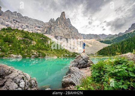 Junger Mann steht auf Stein, Wanderer am türkisgrünen Sorapis-See, Lago di Sorapis, Berggipfel Dito di Dio, in den Dolmen, Belluno, Italien Stockfoto