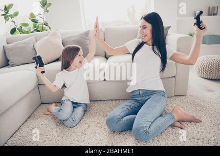 Foto in voller Größe von der entzückenden Mama, kleines Kind, Sit Harmony, Komfort-Sofa, Barfuß, Spielstation, Win Game Show, hoch fünf Zeichen, die Hände im Zimmer klatschen Stockfoto