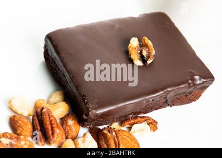 Köstliche Schokoladen-Fudge-Brownie und Walnussgarnieren oben; auf weißer Platte mit gemischten Nüssen Stockfoto