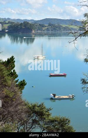 Vertikaler Blick auf drei Boote, die in einem flachen, ruhigen Hafen mit Hügeln im Hintergrund verankert sind. Stockfoto