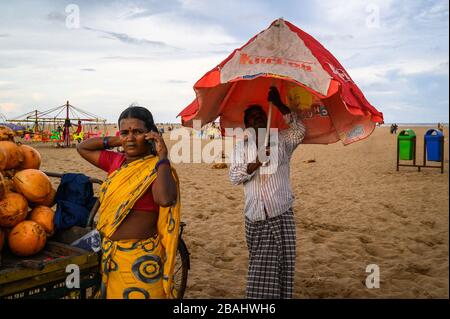 Mann eröffnet einen Regenschirm, während seine Frau telefoniert, Marina Beach, Chennai, Indien Stockfoto