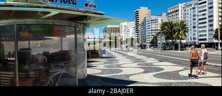 Panorama des geschlossenen Kioskstandes mit einem älteren Paar, das am Mittag beim COVID-19 Corona-Virus auf dem Copacabana-Boulevard vorbeigeht Stockfoto