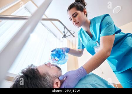 Unter der Ansicht der jungen Krankenschwester in Schruben und chirurgischen Handschuhen mit der Maske für die Beutelventile während der manuellen Beatmung Stockfoto