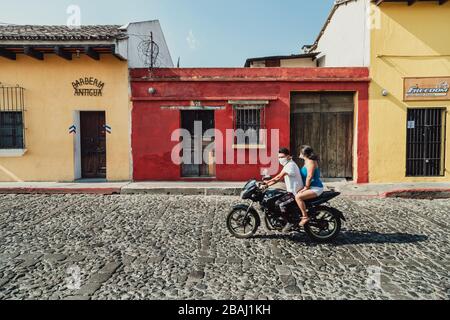 Das Paar trägt während der Coronavirus-Pandemie Gesichtsmasken auf dem Motorrad. Leere Straßen in der farbenfrohen Kolonialstadt Antigua Guatemala Stockfoto