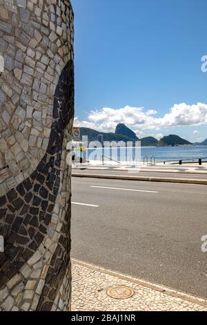 Dekorative Wand mit portugiesischen Fliesenwellen mit dem Berg Sugarloaf hinter einer leeren Straße, einem Boulevard und einem Strand in Copacabana Stockfoto