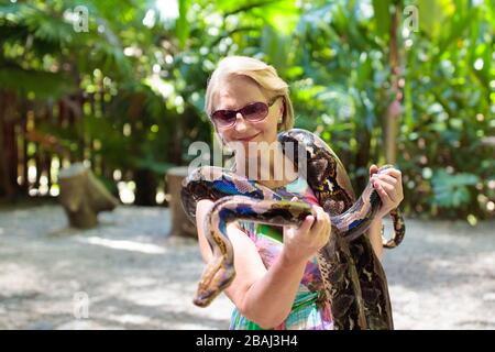 Frau mit python Schlange in Tropical Zoo. Dame beobachten exotische Reptil. Weibliche Touristen mit Schlangen auf Reise Park zu Safari. Menschen beim Lernen zu overco Stockfoto