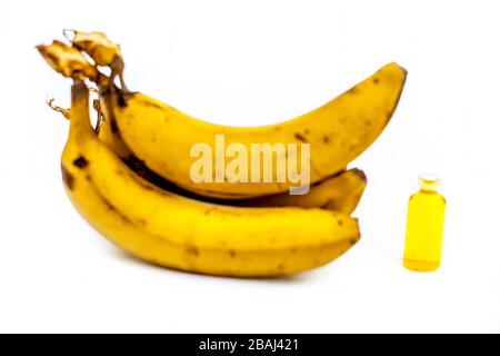 Nahaufnahme von Bananenöl in einer Glasflasche oder Isoamylacetat zusammen mit frischen gelben Bananen, die auf Weiß isoliert sind. Stockfoto