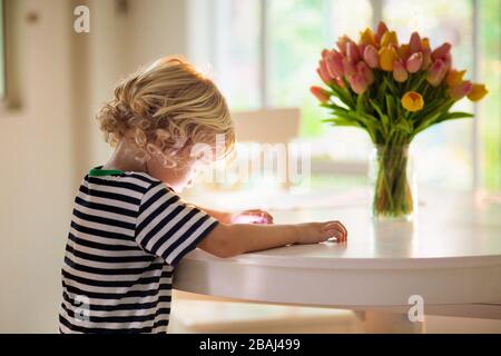 Kind mit Tablet-pc. Kinder mit Computer. Online-Spiele. Kleiner Junge am Esstisch, der auf Laptop oder Pad spielt. Stockfoto