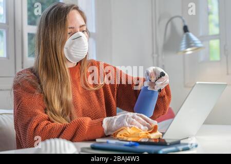 Coronavirus. Frau mit Gesichtsmaske und Gummihandschuhen, die während der Coronavirus-Epidemie zu Hause ihren Arbeitsplatz mit einem Desinfektionsmittel säubert. Prävention Stockfoto