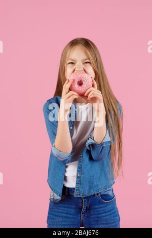 Mädchen, die mit einem Donut auf einem rosafarbenen Hintergrund spielen Stockfoto