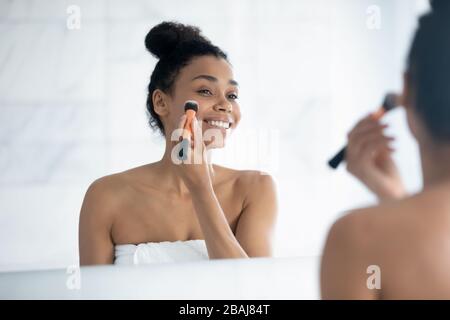 Schöne afrikanerin hält Bürste, die das Fundament auf dem Gesicht aufträgt Stockfoto