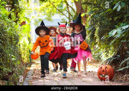Kind in Halloween-Kostüm. Asiatische und kaukasische Kinder mit gemischten Rassen tricksen oder gönnen sich auf der Vorstadtstraße. Kleiner Junge und Mädchen mit Kürbislaterne und Süßigkeiten Stockfoto