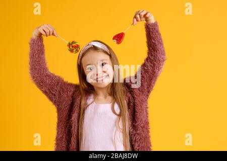 Kleine Mädchen genießen während der Schulpause Lollipops. Glückliche kleine Schüler essen Lollipops. Große wirbelnde Lollipops auf Stöcken Stockfoto