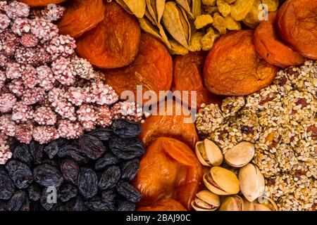 Verschiedene Nüsse und Trockenfrüchte, Aprikosen, Rosinen, Sesam in runder Form auf Betongrund, Zink, Eisen, Magnesium, Mangan, phosphorreiche Lebensmittel Stockfoto